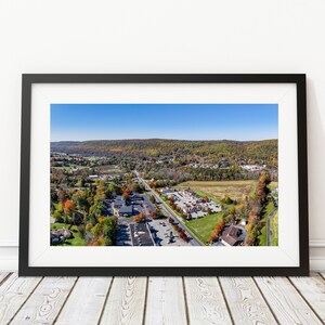 May include: Aerial view of a small town in the fall with colorful trees and a blue sky. The town has a mix of residential and commercial buildings.