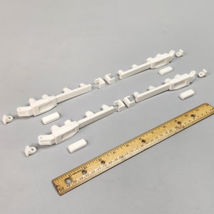 May include: Two white plastic model train track sections with connecting pieces. The track sections are about 12 inches long and have a ruler in the background for scale.