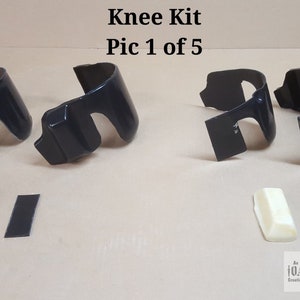 May include: A set of four black knee pads for motorcycles. The set includes two knee pads, two foam pads, and two black strips. The knee pads are made of a hard plastic material and have a curved shape. The foam pads are white and are designed to be placed under the knee pads for added comfort. The black strips are designed to be attached to the knee pads to help keep them in place.