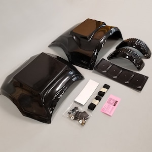 Puede incluir: Un conjunto de piezas de carrocer&iacute;a de coche de pl&aacute;stico negro para un coche modelo. El conjunto incluye dos paneles de carrocer&iacute;a grandes, dos pasos de rueda m&aacute;s peque&ntilde;os, una pieza plana con cuatro agujeros y una peque&ntilde;a bolsa de sujetadores. El conjunto tambi&eacute;n incluye dos correas negras y una hoja de instrucciones rosa.