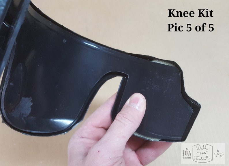 May include: Close-up of a black knee brace with a cutout for the kneecap. The brace is made of a flexible material and has a soft lining. The brace is being held by a hand. The text "Will Stitch" is visible on the brace.