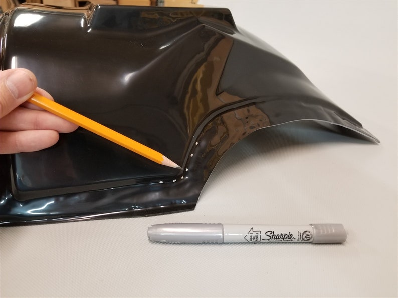 Puede incluir: Una pieza de pl&aacute;stico negro con una fila de puntos blancos a lo largo del borde. Una persona est&aacute; usando un l&aacute;piz amarillo para trazar los puntos. Un marcador plateado Sharpie est&aacute; sobre la superficie.