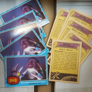 May include: A stack of yellow and brown trading cards with a blue and white card on top. The card features a man wearing a blue shirt and holding a ring. The text on the card reads "Will Friedrichs was Red Krayt Dragon! In Memory 1971-2017". The text on the yellow and brown cards reads "Imperial Outpost Armory 08/23/71 - 08/11/17".