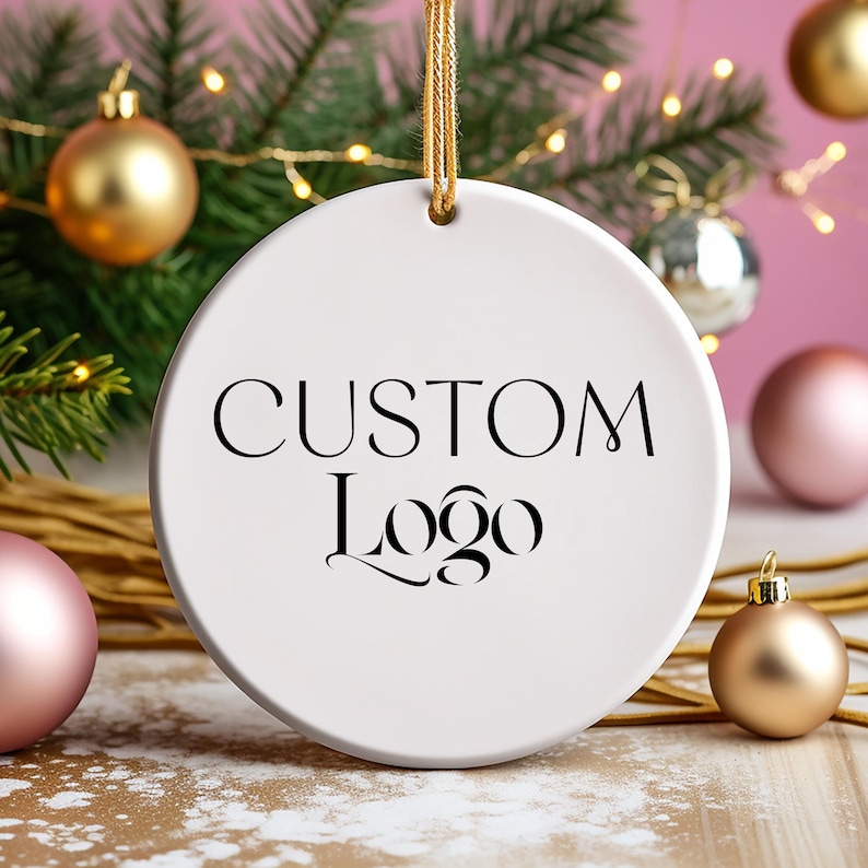 May include: White ceramic ornament with a gold string for hanging. The ornament has black text that reads "CUSTOM Logo".
