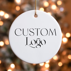 May include: White ceramic Christmas ornament with a black inscription that reads "CUSTOM Logo".