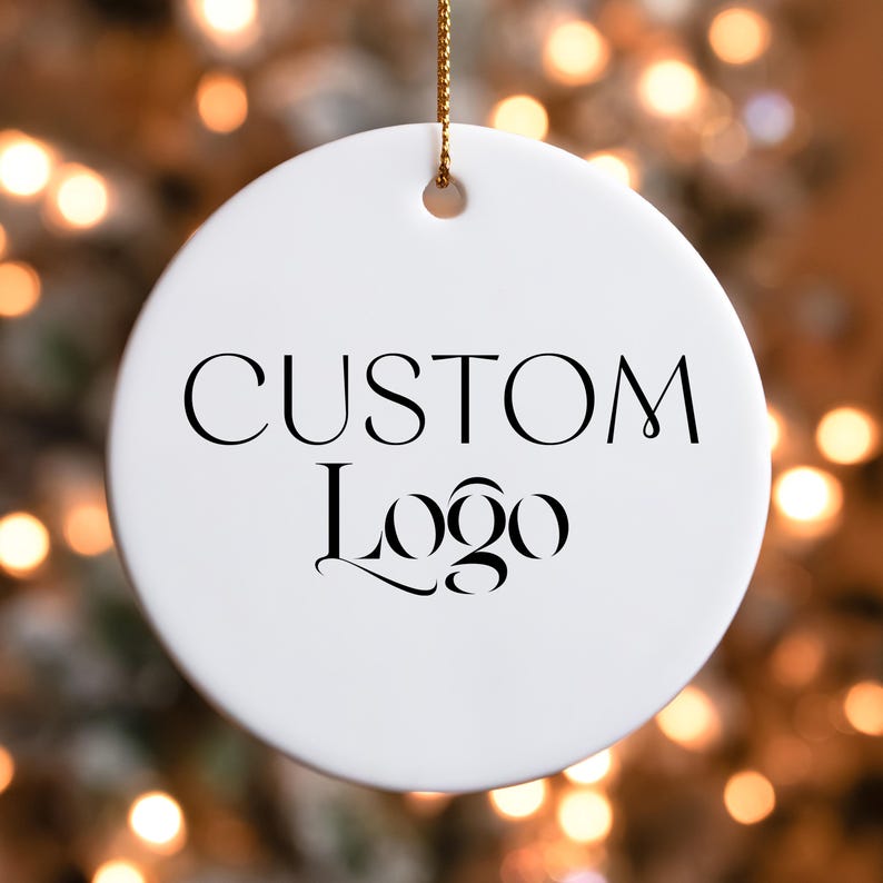 May include: White ceramic Christmas ornament with a black inscription that reads "CUSTOM Logo".