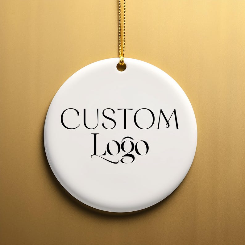 May include: White ceramic ornament with a gold string for hanging. The ornament has black text that reads "CUSTOM Logo".