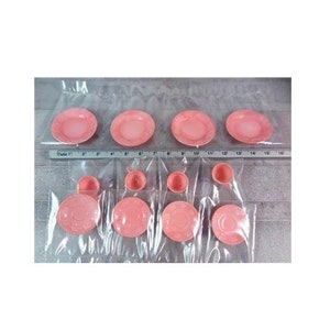 May include: A set of pink plastic teacups and saucers. The set includes four teacups and four saucers, all in a pale pink color. The teacups and saucers are decorated with a simple, elegant design.