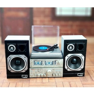 Puede incluir: Un sistema estéreo vintage con un tocadiscos, un amplificador y dos altavoces negros. El tocadiscos tiene un disco azul. El amplificador y los altavoces tienen detalles plateados y negros. El sistema está sobre una superficie de madera.