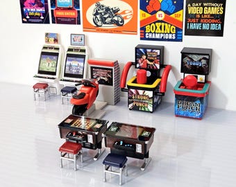 May include: A collection of miniature arcade game machines, including a boxing game, a motorcycle racing game, and a punching game. The games are all brightly coloured and feature various graphics, including a red motorcycle, a boxing ring, and a punching bag. The games are arranged on a white surface with a few small stools.