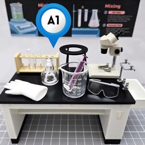 Op de afbeelding: Een miniatuur laboratoriumwerkbankset met een zwart tafelblad, een doorzichtige glazen beker met een paarse injectiespuit, een witte handschoen, een reageerbuisrek, een glazen fles, een veiligheidsbril en een microscoop, met een blauwe A1-locatiemarkering.
