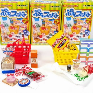 May include: Two miniature shopping baskets filled with various miniature grocery items, including a bag of chips, a loaf of bread, a can of soup, and a box of milk. The baskets are on a white surface with a white background. The boxes are labeled "プチスーパー" which translates to "Mini Supermarket".