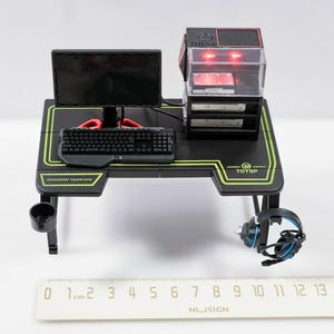Puede incluir: Un escritorio de juego negro con un diseño verde y negro. El escritorio tiene un monitor, un teclado y una torre de ordenador. La torre de ordenador tiene una luz roja en la parte delantera. El escritorio también tiene un soporte para auriculares y un portavasos.