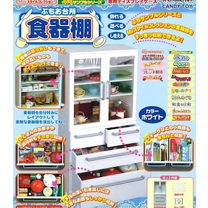 Puede incluir: Un armario de cocina blanco con puertas de vidrio y cajones. El armario está lleno de platos en miniatura, tazas y otros artículos de cocina. El texto en la imagen dice "ぷちお台所 食器棚", que se traduce como "Mini Armario de Cocina".
