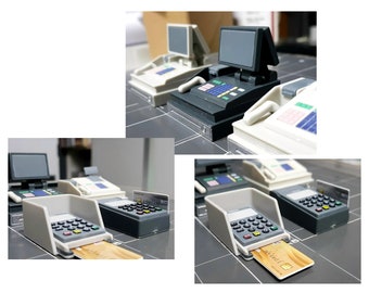 May include: A set of four miniature cash registers, including a black and white register with a small monitor, a white register with a black monitor, and two smaller white registers with card readers. The registers are made of plastic and are designed to look like real cash registers.