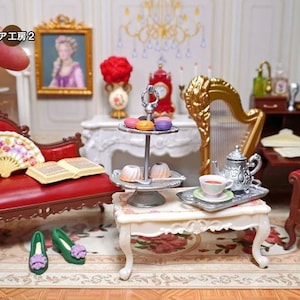 Könnte beinhalten: Ein Miniatur-Wohnzimmer-Set für ein Puppenhaus mit einer roten Samt-Chaiselongue, einem Fächer, einem Buch, einem kleinen Tisch mit einem silbernen Tablett, einer Teekanne, einer Tasse und einem Untertasse, einer Harfe und einem roten Samt-Sessel mit einer Krone.