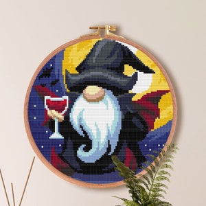 May include: Cross stitch pattern of a gnome dressed as a vampire holding a glass of wine. The gnome is wearing a black hat and cape. The background is a dark blue with stars and a crescent moon. The pattern is for Aida cloth with 14 count. The pattern is 100 stitches by 100 stitches, or 7.1 inches by 7.1 inches.