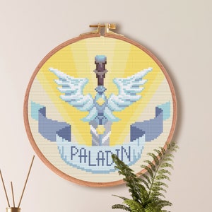 以下が含まれることがあります： 「PALADIN」と書かれたバナーと翼のある剣のクロスステッチパターン。パターンは木製の輪で囲まれ、黄色の背景の壁に飾られています。