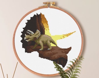 May include: Cross stitch pattern of a brown and green dinosaur with a yellow background. The pattern is in a wooden embroidery hoop. The text below the hoop reads "Size For Aida (14) 100X98 Stitches | 7.1"X7" | 18.1' X 17.8 cm" and "Color Palette 17 DMC Colors".