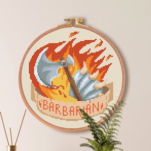 May include: Cross-stitch pattern of a barbarian holding an axe in flames, with the word "BARBARIAN" written below. The pattern is framed in a round wooden hoop and is 7.1 inches by 7.1 inches.