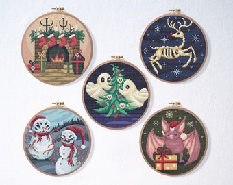 May include: Five round embroidery hoops with different holiday-themed cross-stitch patterns. The patterns include a fireplace with stockings, a Christmas tree with ghosts, a skeleton reindeer, a snowman, and a bat with a gift.