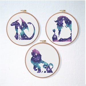 May include: Three embroidery hoops with galaxy-themed cross-stitch patterns. The first hoop features a silhouette of a dragon and a person, the second hoop features a silhouette of a princess and a prince, and the third hoop features a silhouette of a lion and a cub.