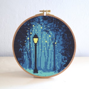 Puede incluir: Un patrón de punto de cruz de una farola en un bosque con un esquema de color azul y verde. La farola está encendida y hay estrellas en el cielo.