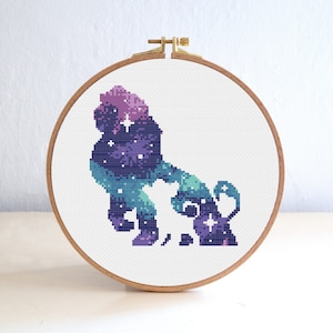 May include: A cross-stitch embroidery hoop with a purple, blue, and green galaxy-themed lion design. The lion is outlined in white and has a few white stars inside the design.