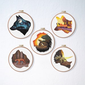 Puede incluir: Cinco aros de bordado con diferentes siluetas de animales. Los aros están en una pared blanca. Los animales son un lobo, un zorro, un león, un tigre y un triceratops.