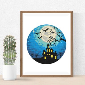 May include: A cross-stitch pattern featuring a spooky silhouette of a haunted house with glowing windows, a full moon, and bats flying in the night sky. The design is framed in a wooden frame.