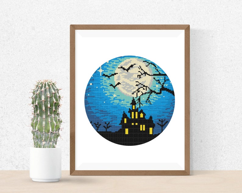 May include: A cross-stitch pattern featuring a spooky silhouette of a haunted house with glowing windows, a full moon, and bats flying in the night sky. The design is framed in a wooden frame.