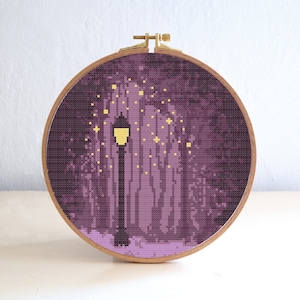 Puede incluir: Un patrón de punto de cruz morado y dorado de una farola en un bosque con un suelo nevado. La farola está encendida y hay estrellas en el cielo.