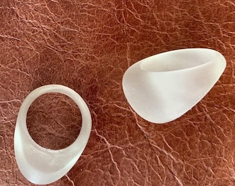Puede incluir: Tres objetos blancos opacos en forma de anillo, hechos de un material liso y duro. Los objetos están dispuestos en forma de triángulo sobre una superficie marrón texturizada.