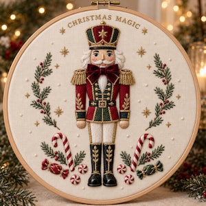 Può includere: Un telaio da ricamo circolare con una figura di schiaccianoci in uniforme rossa, verde e dorata con un fiocco di velluto. Il testo CHRISTMAS MAGIC è ricamato in alto, circondato da rami di pino, bastoncini di zucchero e piccole stelle.