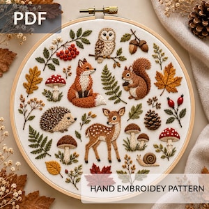 May include: A circular embroidery hoop containing a white fabric panel with a detailed hand embroidery pattern featuring a fox, a deer, a hedgehog, an owl, a squirrel, a snail, mushrooms, autumn leaves, acorns, and berries.