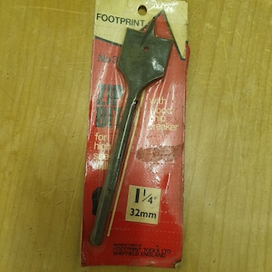 May include: A black wood drill bit with a red and white label that says "Footprint" and "1/4" 32mm. The label also says "with wood chip breaker".