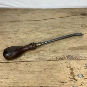 Puede incluir: Una herramienta vintage de metal con mango de madera y hoja curva. La herramienta está hecha de metal y madera y tiene un acento de latón.