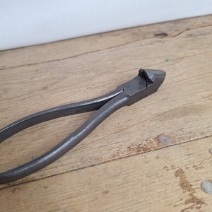 Puede incluir: Un par de alicates de metal vintage con una punta puntiaguda, que se encuentran sobre una superficie de madera.