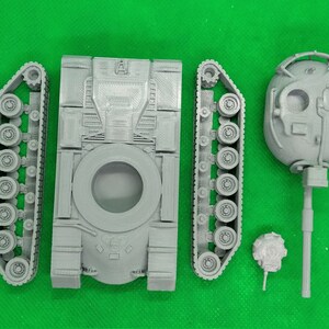 May include: A gray plastic model kit of a tank, with separate pieces for the body, tracks, and turret. The turret has a detailed design with a small hatch and a barrel.