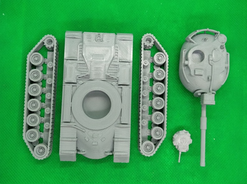 May include: A gray plastic model kit of a tank, with separate pieces for the body, tracks, and turret. The turret has a detailed design with a small hatch and a barrel.