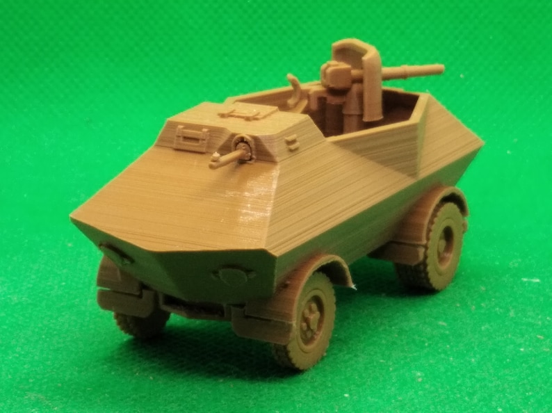 May include: A brown plastic model of a military armored car with a rotating turret and a machine gun. The car has four wheels and is on a green surface.