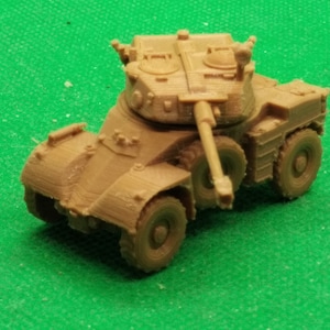 Op de afbeelding: Een bruin plastic model van een militaire gepantserde auto met een draaibare toren en een kanon. De auto heeft vier wielen en staat op een groene ondergrond.