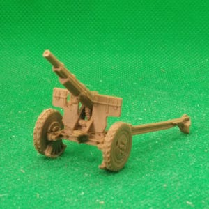 Puede incluir: Un modelo de pieza de artillería de color beige con dos ruedas, un cañón largo y un afuste detallado. El cañón en miniatura se encuentra sobre un fondo verde, mostrando su diseño y estructura. Este modelo es probablemente para coleccionistas o aficionados.