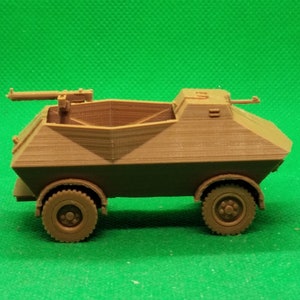 May include: A brown plastic model of a military armored car with a machine gun mounted on top. The car has four wheels and a rectangular body.