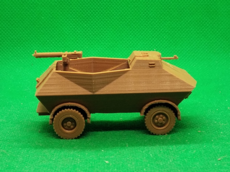 May include: A brown plastic model of a military armored car with a machine gun mounted on top. The car has four wheels and a rectangular body.