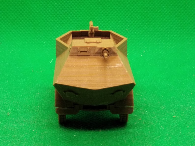 May include: A brown plastic model of a military armored car with a gun turret on top. The model is detailed with a textured surface and a raised gun barrel.