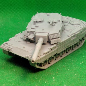 Puede incluir: Un modelo de tanque gris con un cañón largo y orugas detalladas. El tanque en miniatura está sobre un fondo verde. El diseño del tanque incluye escotillas y otras características realistas, mostrando un vehículo militar.
