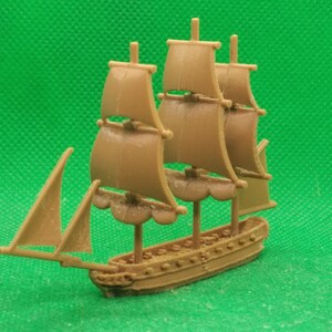 May include: A miniature brown toy sailboat with three masts and sails. The ship has a detailed hull with decorative elements and is set against a green background. The toy is a model of a sailing vessel.