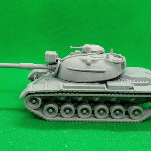May include: A gray plastic model of a tank with a large cannon and tracks. The tank is on a green background.
