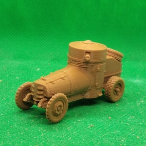 May include: A tan model of an armoured car, with a cylindrical turret and a boxy rear. The vehicle has four wheels and is set against a green background. The model is a miniature replica of a historical military vehicle, likely for collectors.